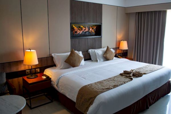 A cozy hotel room with a large bed, two bedside tables with lamps, wall art, and a window with curtains letting in natural light.