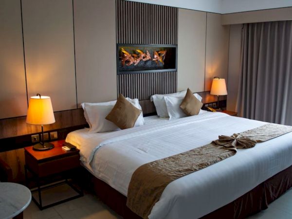 A cozy hotel room with a large bed, two bedside tables with lamps, wall art, and a window with curtains letting in natural light.