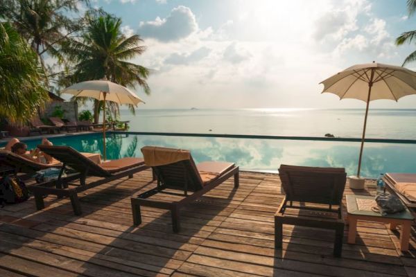A serene beachside setting with lounge chairs, umbrellas, and a wooden deck overlooking a calm sea and a view of the sunset or sunrise.