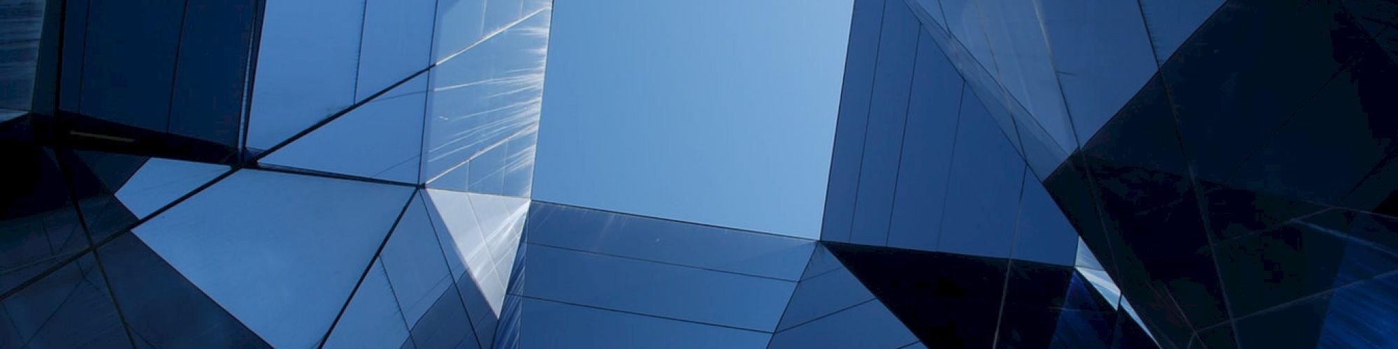 View of a modern glass building's inner courtyard, with reflective surfaces and geometric shapes leading to the sky.