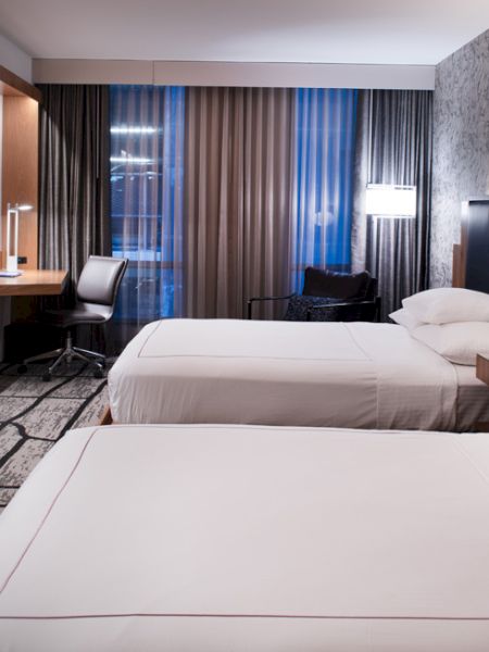 A modern hotel room with two neatly made beds, a desk with a chair, a flat-screen TV on the wall, and contemporary decor ending the sentence.