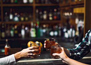 Three people toasting with drinks in a bar with shelves of bottles in the background.