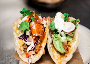 The image shows two tacos filled with ingredients like meat, lettuce, cilantro, and sour cream, garnished with radish slices on a plate.