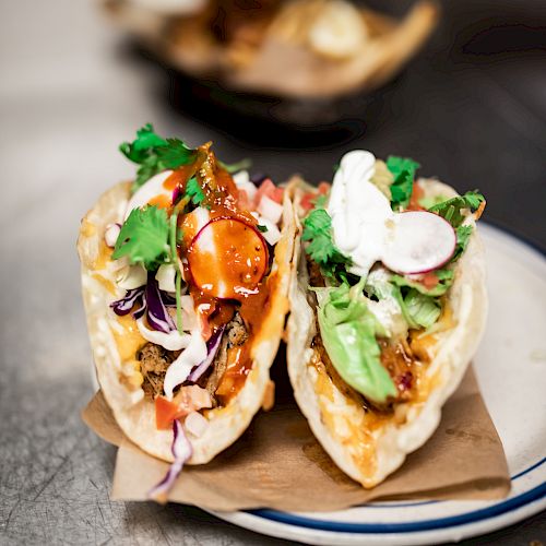 The image shows two tacos filled with ingredients like meat, lettuce, cilantro, and sour cream, garnished with radish slices on a plate.