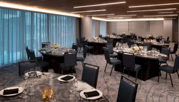 The image shows an elegantly set banquet hall with round tables covered in black cloths, set with glasses, plates, and floral centerpieces.