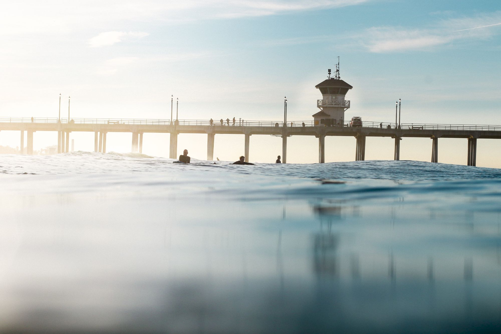 A peaceful ocean scene with a pier and a few people in the water, under a clear sky.